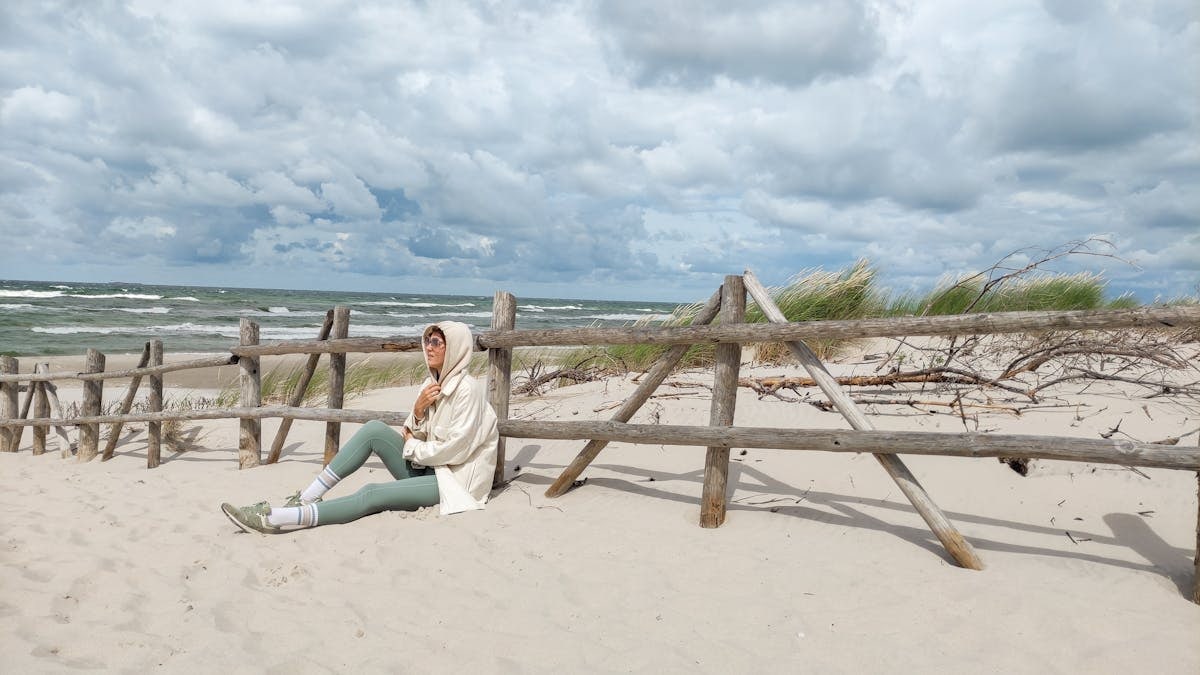 Person in casual attire sits on Baltic beach, enjoying the serene sea view.